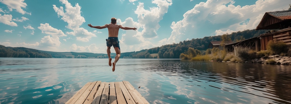Jonge man springt vanaf de steiger in het meer.