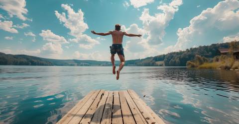 Jonge man springt vanaf de steiger in het meer.